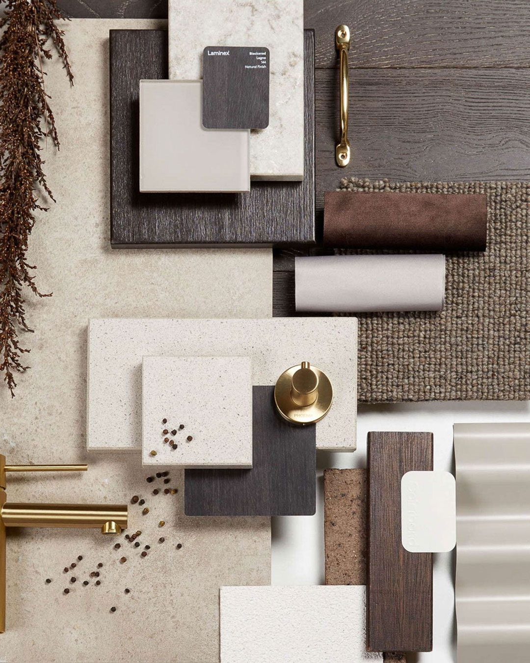 Various material samples, including wood, laminate, fabric, and metal hardware, are arranged on a surface. Some dried plant stems and seeds are also included for decor.