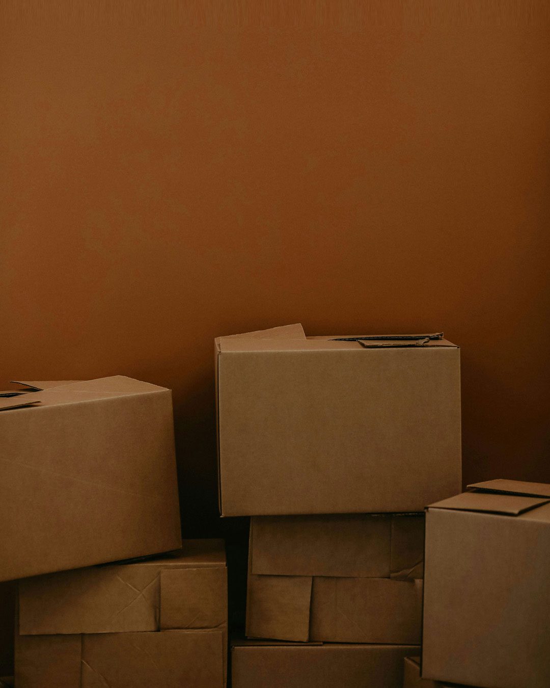 A stack of closed cardboard boxes against a plain brown background.