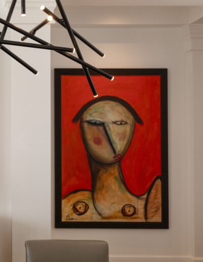 Painting of an abstract human figure with red background, displayed on a wall next to a modern chandelier.