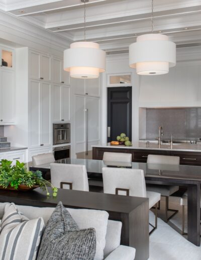 Modern kitchen and dining area featuring white cabinetry, double pendant lights over a central island with a sink, and a nearby dining table with grey upholstered chairs.