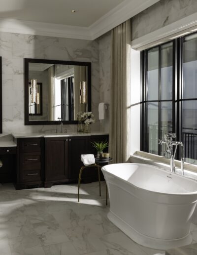 Luxurious bathroom with marble floor and walls, freestanding bathtub beside large windows with a view, double vanity with mirrors, and glass-enclosed shower. Modern décor and fixtures throughout.